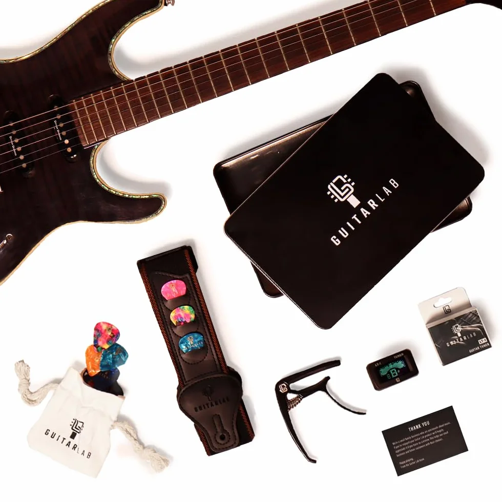 Pudełko prezentowe z akcesoriami gitarowymi [marki Guitar Lab], metalowa puszka zawiera pasek do gitary, kapodaster, elektroniczny tuner i puszkę, idealne dla miłośników gitary i uczących się gry